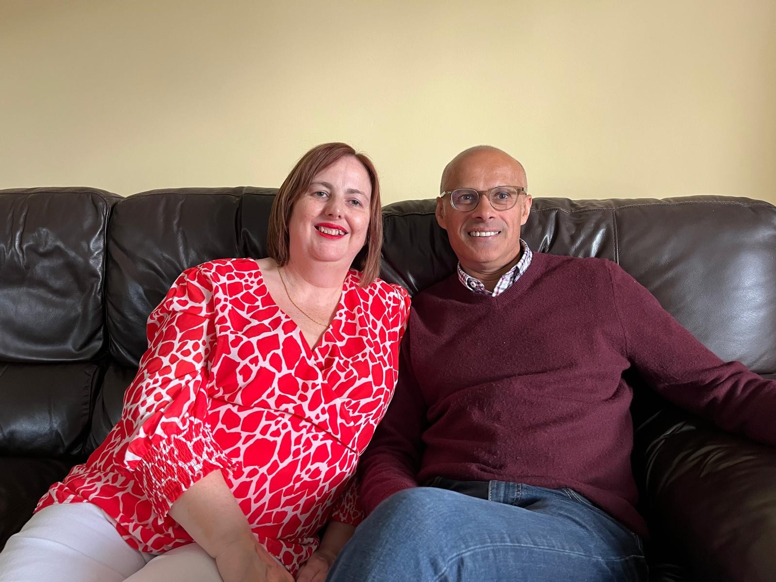Suzanne and Boo relax on their couch at home. Both smile and look very happy.