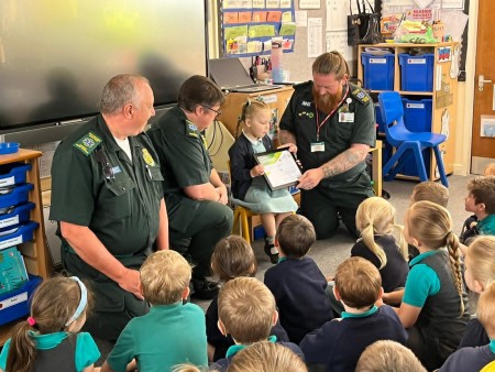 Lola is presented her award by the ambulance crew in her class in front of her class mates