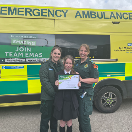 Brooke Clements holds her certificate while standing in between Sophie Littlefair and Lisa Doyle. They alre all smiling, while stood in front of an EMAS ambulance.