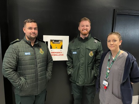 Lee McLaren and Jordan Griffiths from EMAS, standing alongside trainee Advanced Clinical Practitioner Naomi Richmond, next to the defibrillator at the gym which was used to help save Richard's life