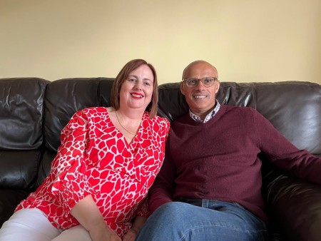 Suzanne and Boo relax on their couch at home. Both smile and look very happy.